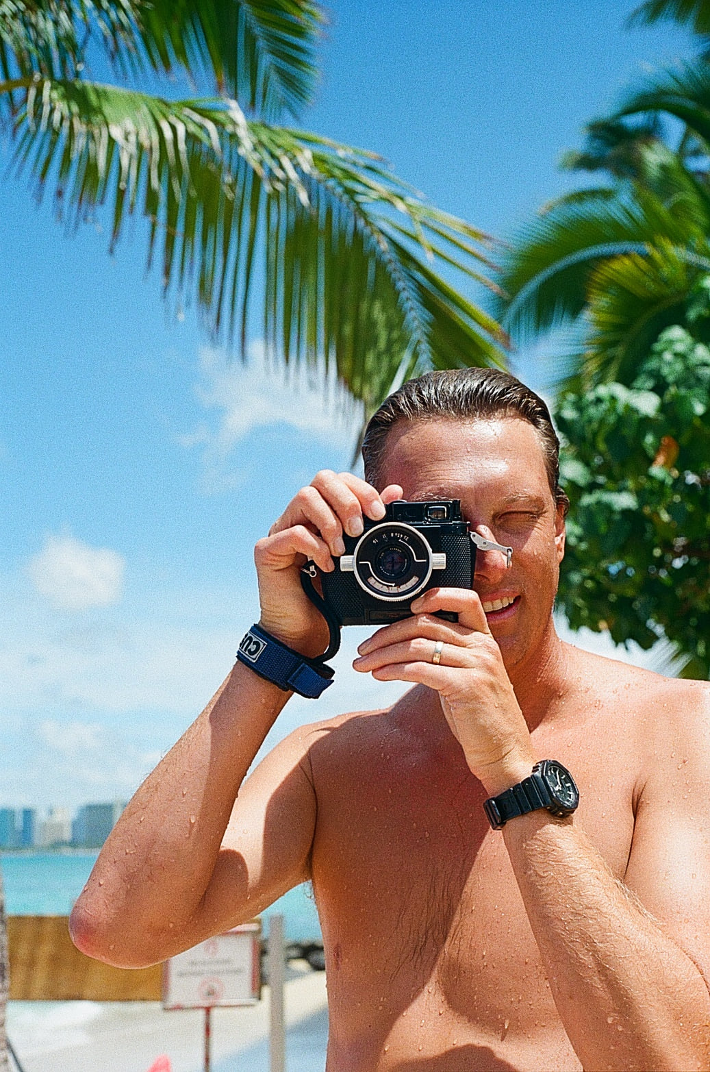 Bryce with the camera at the shore, palms and open water behind him.